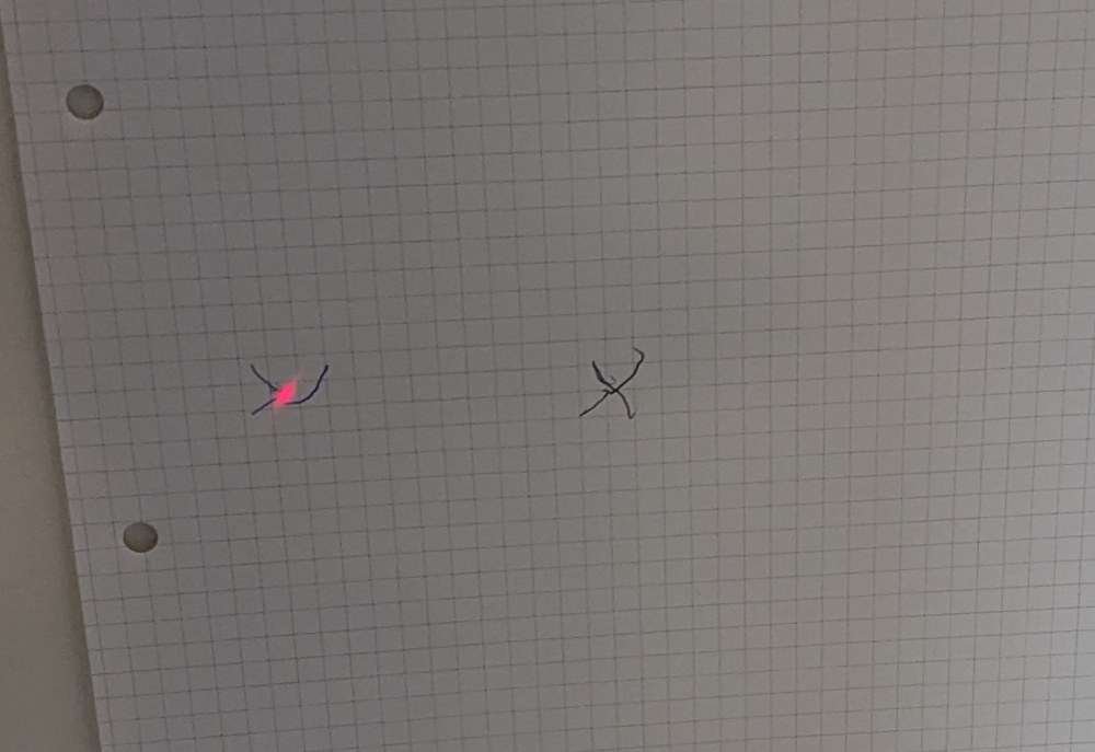 Graph paper on the right wall with two pencil crosses, the red laser dot on the left one